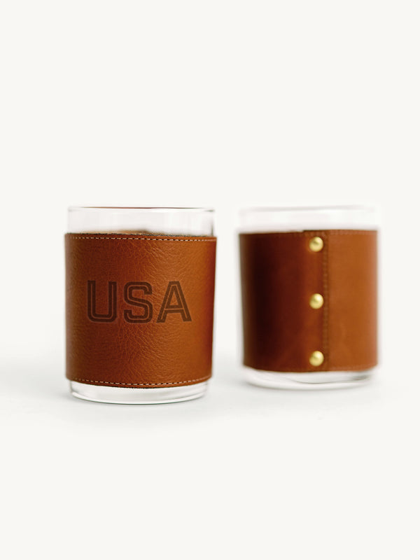 Two glass tumblers with brown leather sleeves, one displaying 'USA'.